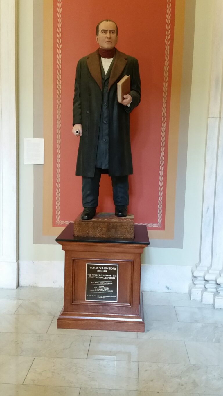 Indoor statue of Thomas Dorr standing and holding a book in one hand and a paper in the other.